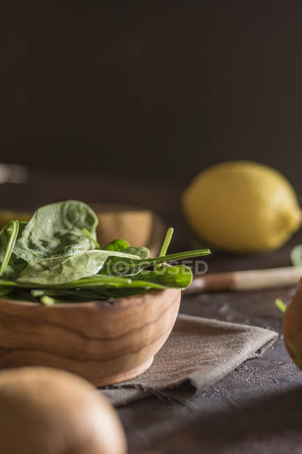 Close up view of bowl with fresh spinach leaves on table with lemons and utensils — Stock Photo