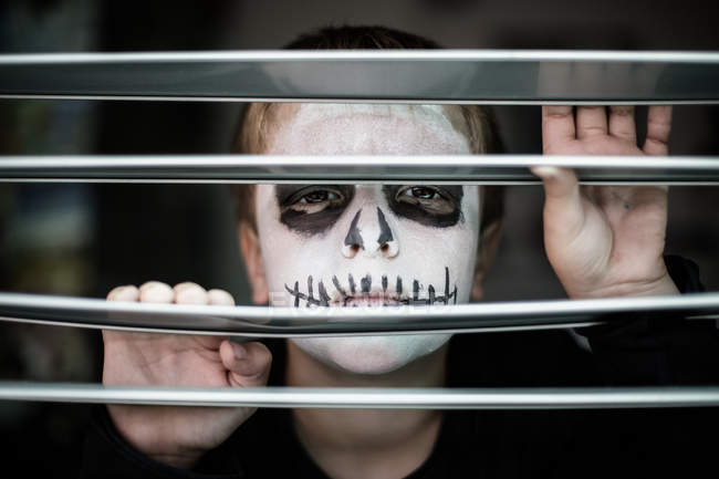Boy with skull face looking through sunblind — Stock Photo