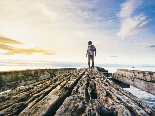 Vista trasera del hombre de pie sobre ruinas de muelle de madera en el fondo del cielo brillante y el mar. - foto de stock
