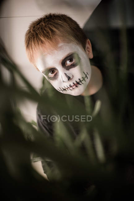 Niño con cara de cráneo escondido detrás de las plantas — Stock Photo