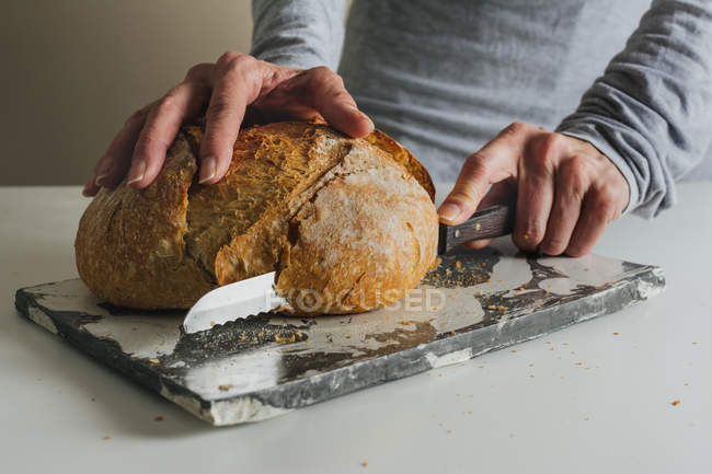 Frau schneidet frisch gebackenes Brot auf Marmortisch — Stockfoto
