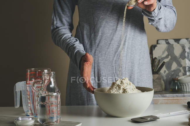 Mãos femininas adicionando levedura para tigela com farinha — Fotografia de Stock