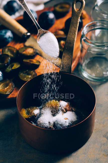 Spoon adding sugar to plums in saucepot — Stock Photo