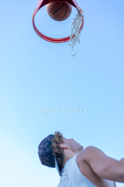Hombre mirando la pelota de baloncesto cayendo a través del anillo - foto de stock