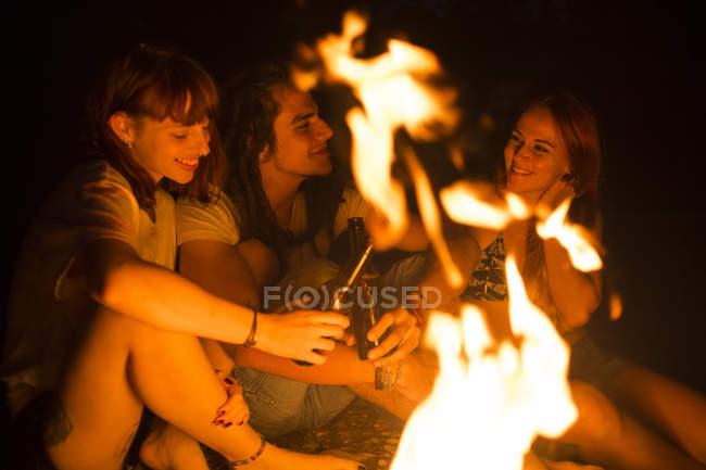 Amigos sentados com cerveja na fogueira — Fotografia de Stock