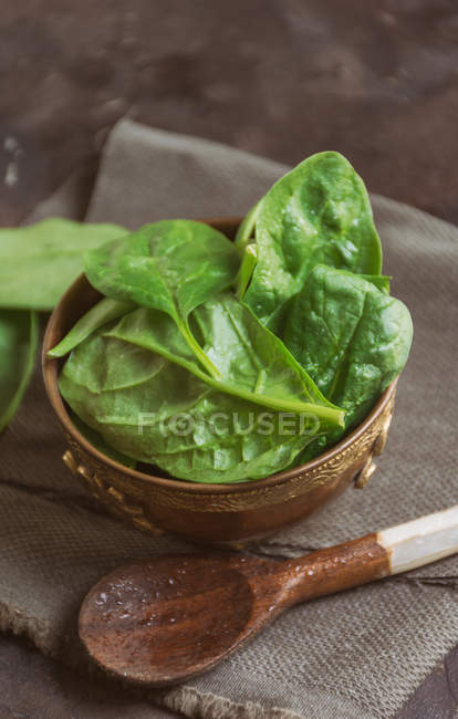 Top view of wooden bowl  filled with fresh spinach leaves with spoon on rural towel — Stock Photo