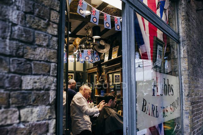 LONDRES, Reino Unido - 4 de mayo de 2017: Disparo a través del vidrio de personas dentro de la barbería con un hermoso diseño . - foto de stock