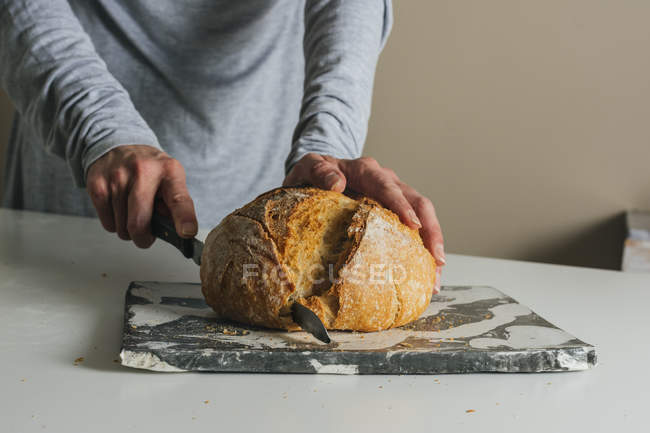 Frau schneidet frisch gebackenes Brot auf Marmortisch — Stockfoto