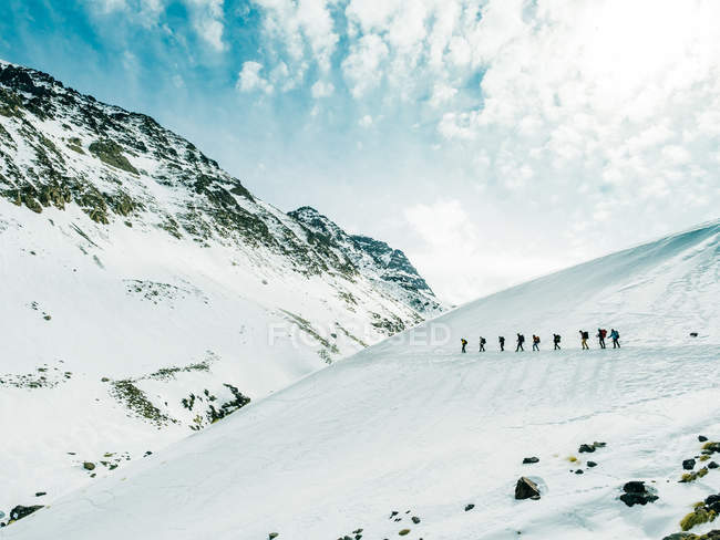 Вид сбоку ряда людей, идущих по склону заснеженных гор — стоковое фото