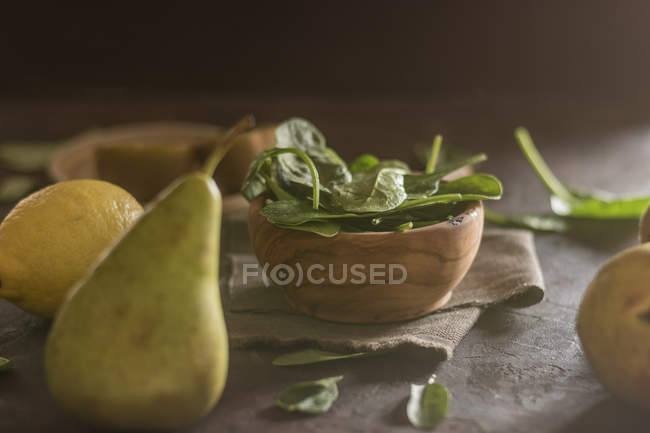 Close up view of wooden bowl with fresh spinach leaves on table with pear, lemon and kiwi — Stock Photo