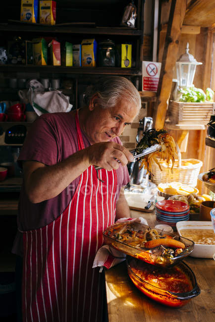 London, Großbritannien - 4. Mai 2017: Reifer Mann in Schürze hält mit Pinzette leckeres gekochtes Essen in der Hand und serviert es auf Teller. — Stockfoto