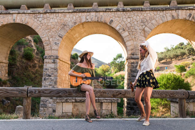 Дівчата з гітарою сидять на сільському паркані — стокове фото