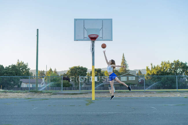 Спортивная женщина в повседневной одежде бросает мяч во время игры в баскетбол на спортивной площадке. — стоковое фото