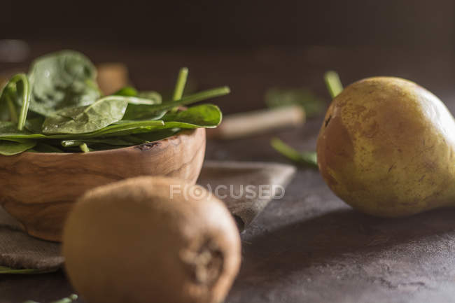 Vista da vicino della ciotola con foglie di spinaci freschi sul tavolo con pera e kiwi — Foto stock