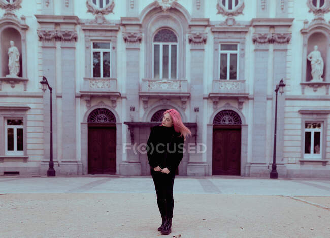 Молодая женщина с розовыми волосами в теплой одежде стоит на городской улице. — стоковое фото