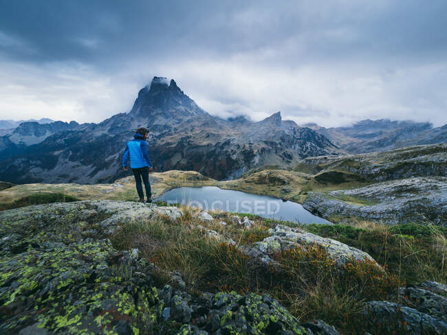 Visão traseira do turista em pé no fundo das montanhas cume e lago calmo sob nuvens. — Fotografia de Stock