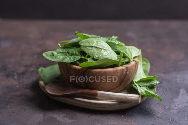 Close up view of wooden bowl filled with fresh spinach leaves and rustic spoon on table — Stock Photo