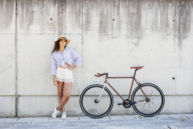 Дівчина в капелюсі позує біля велосипеда — стокове фото
