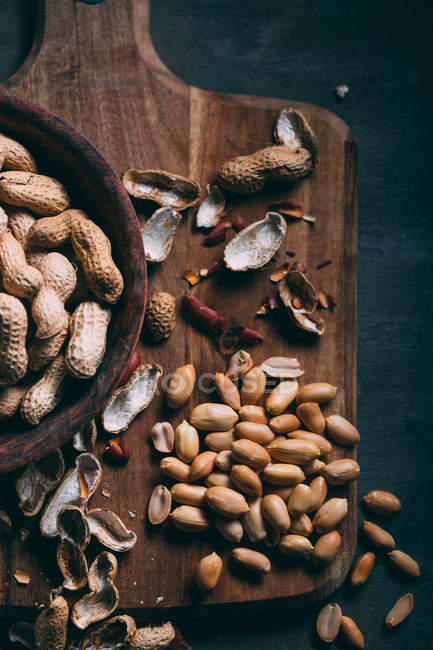 Vue rapprochée des cacahuètes dans un bol en bois sur une planche à découper sur fond sombre — Photo de stock