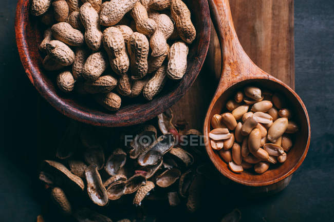 Vue du dessus des cacahuètes dans une cuillère et un bol en bois sur une planche à découper — Photo de stock