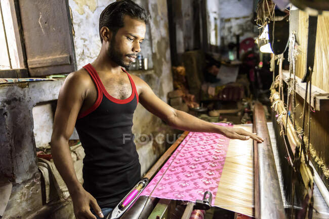Vista lateral do jovem indiano de pé e trabalhando com tecido na loja. — Fotografia de Stock