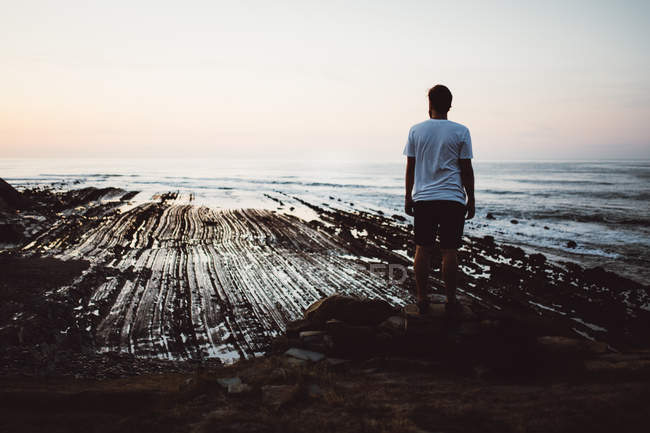Rückansicht eines Mannes, der an der Küste auf einem Felsen posiert — Stockfoto