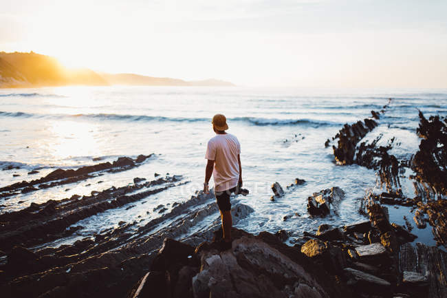 Visão traseira do homem com câmera posando na rocha costeira — Fotografia de Stock