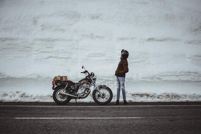 Man in alaska jacket standing by motorcycle in snowy road — Stock Photo