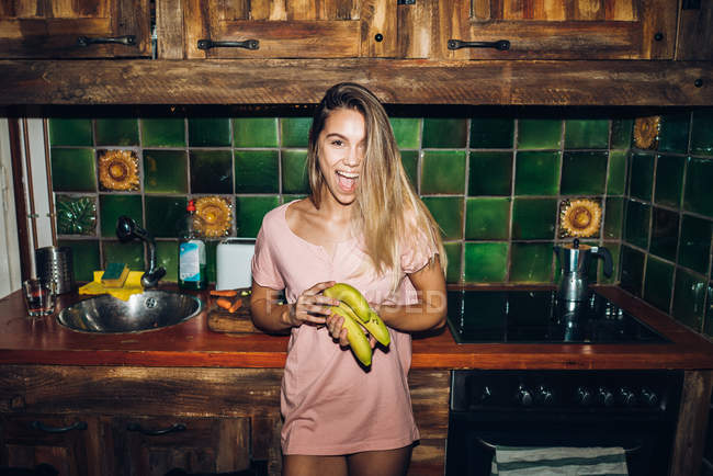 Portrait of cheerful girl holding bananas at kitchen — Stock Photo