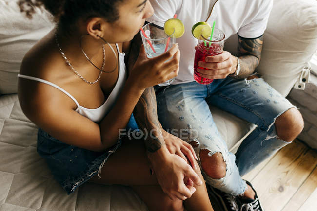 Crop couple sitting with cocktails on sofa — Stock Photo
