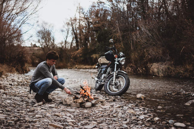 Side view of traveler keeping camp fire by parked motorcycle — Stock Photo