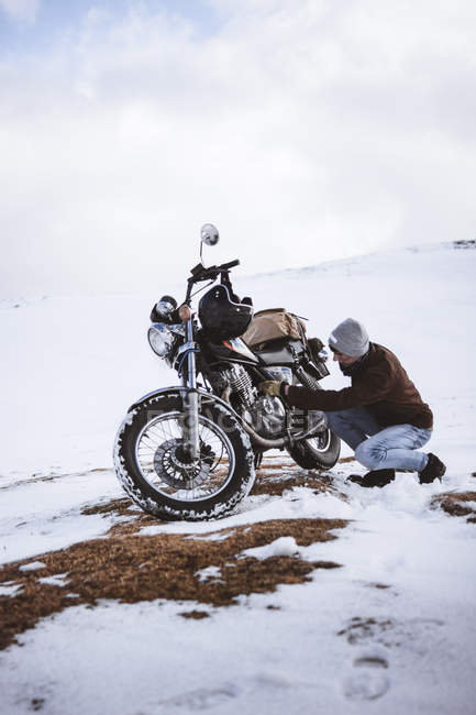 Homem ajustando o motor da motocicleta em montanhas nevadas — Fotografia de Stock