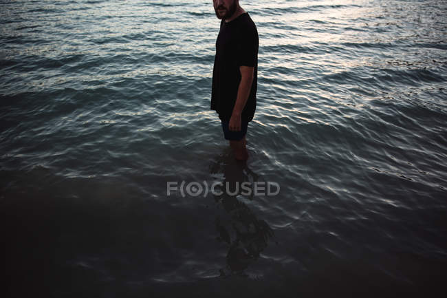 Crop Man in schwarzem T-Shirt und kurzer Hose steht knietief im Wasser. — Stockfoto