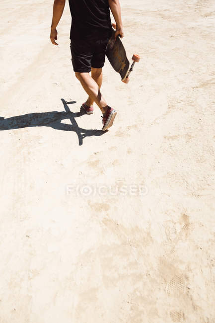Crop man walking with skateboard in desert — Stock Photo