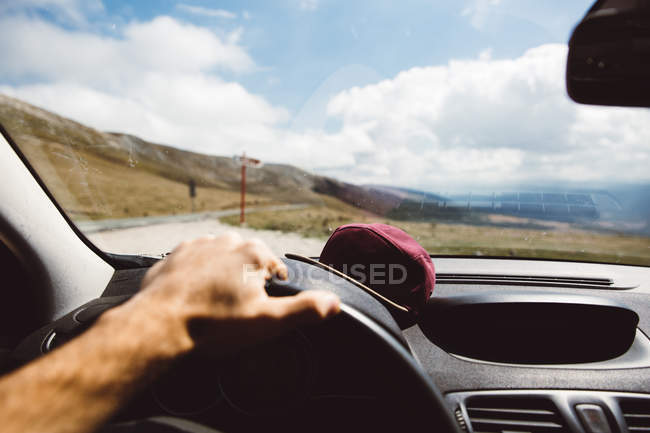 Crop mão no volante carro de condução na estrada em montanhas no dia ensolarado . — Fotografia de Stock