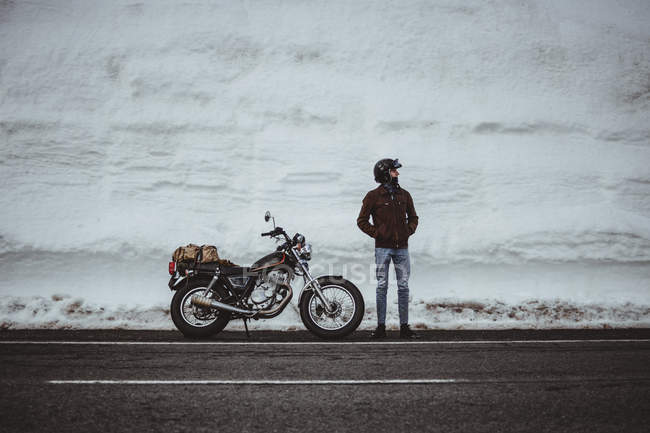 Чоловік в шоломі позує на мотоциклі в засніженій дорозі — стокове фото