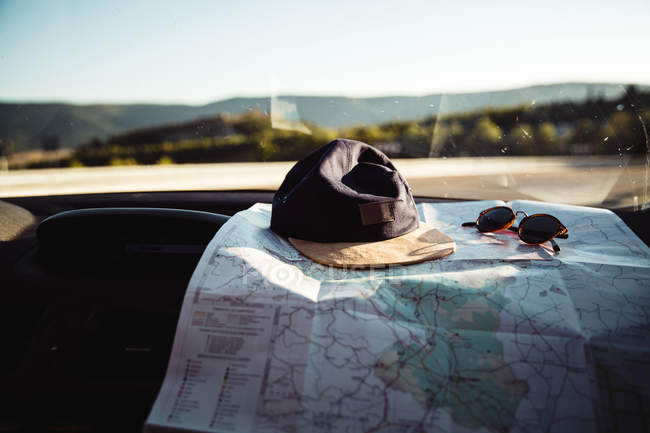 Close up view of cap with sunglasses lying on map at dashboard in car. — Stock Photo