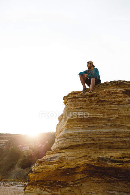Homem turístico sentado em um penhasco iluminado e olhando para longe — Fotografia de Stock