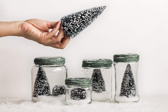 Crop of female hand holding decorative Christmas tree over jars with christmas decorations — Stock Photo