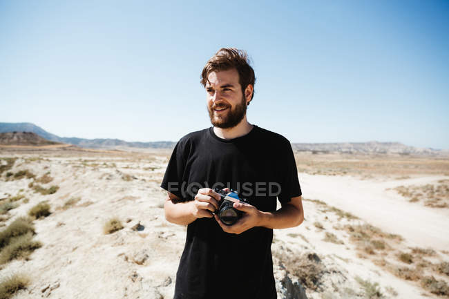 Ritratto di uomo barbuto in posa con macchina fotografica sul deserto — Foto stock