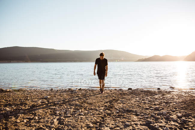 Homem andando na praia iluminada pelo sol sobre colinas enevoadas no fundo — Fotografia de Stock