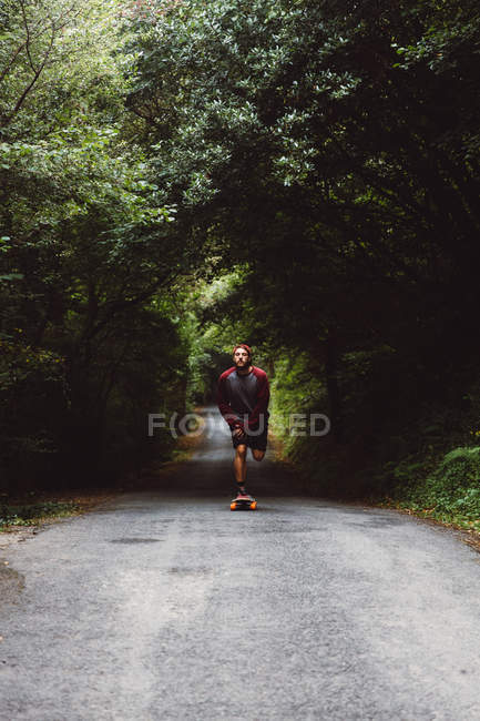 Vista frontale dell'uomo che si libera sullo skateboard sulla strada forestale — Foto stock