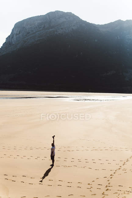 Low angle distant view of man extending arm with camera on beach — Stock Photo