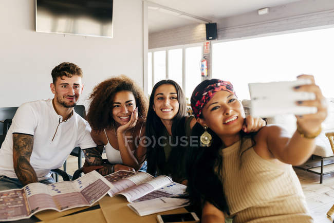 Groupe joyeux d'amis assis dans un café ensemble et prenant selfie avec smartphone . — Photo de stock