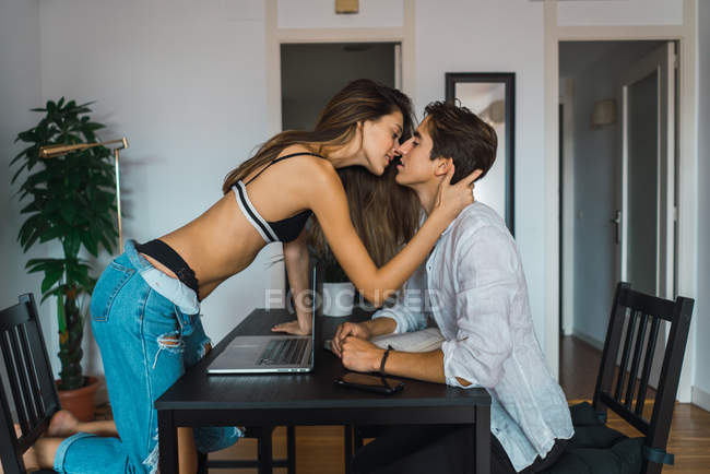 Вид сбоку чувственной пары, целующейся над столом с ноутбуком — стоковое фото