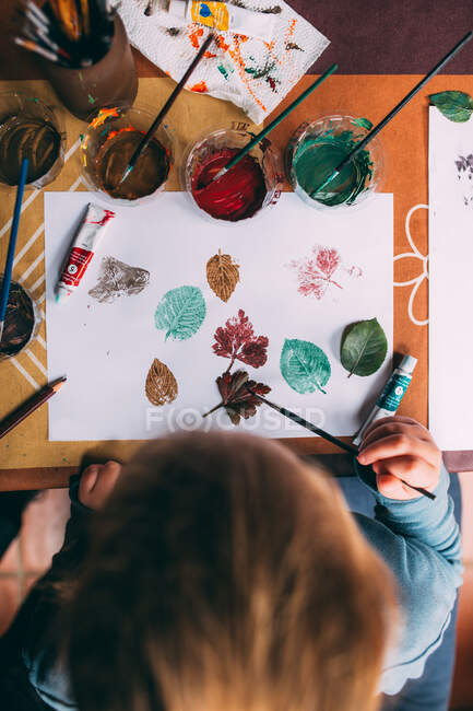 Girl painting leaves and stamping them in paper — Stock Photo