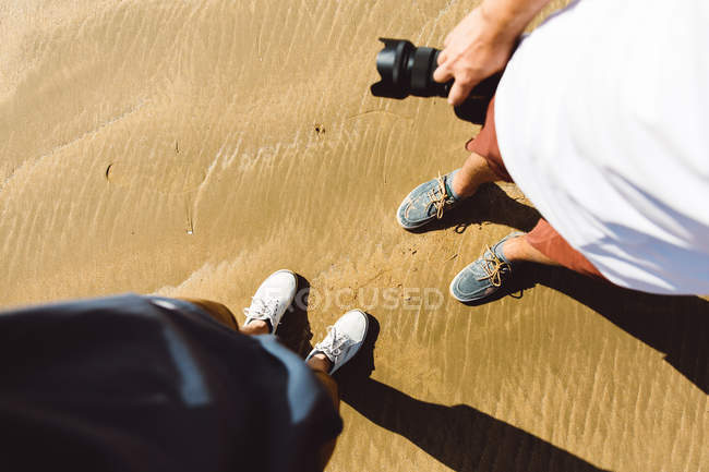 Vue en bas de deux personnes debout sur du sable mouillé avec du sable — Photo de stock