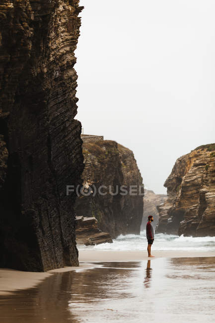 Vista laterale di uomo barbuto in piedi a scogliere cala e guardando l'oceano
. — Foto stock