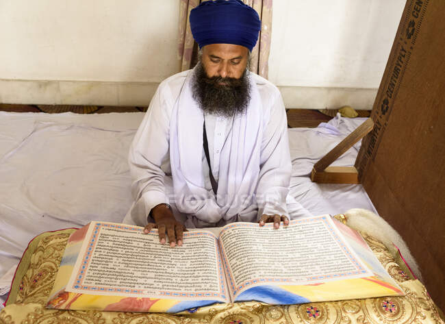 Homme indien en blanc vêtements traditionnels assis et la lecture énorme livre. — Photo de stock