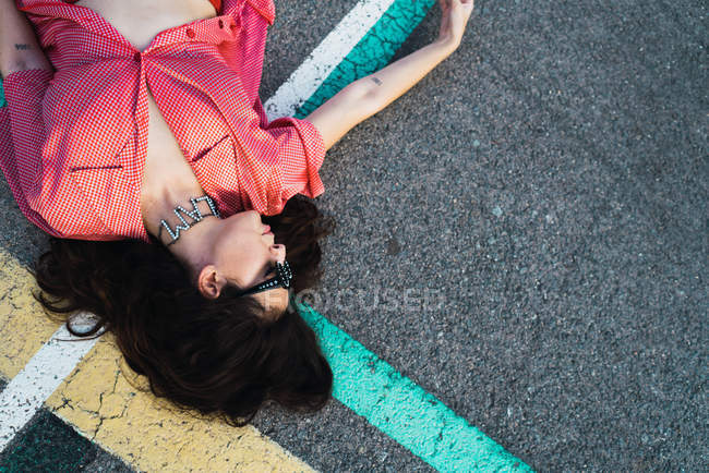 Top view of brunette in sunglasses lying on asphalt — Stock Photo